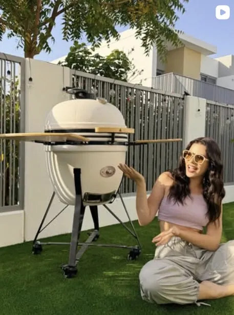 A woman sitting on the grass next to a white kamado outside a villa